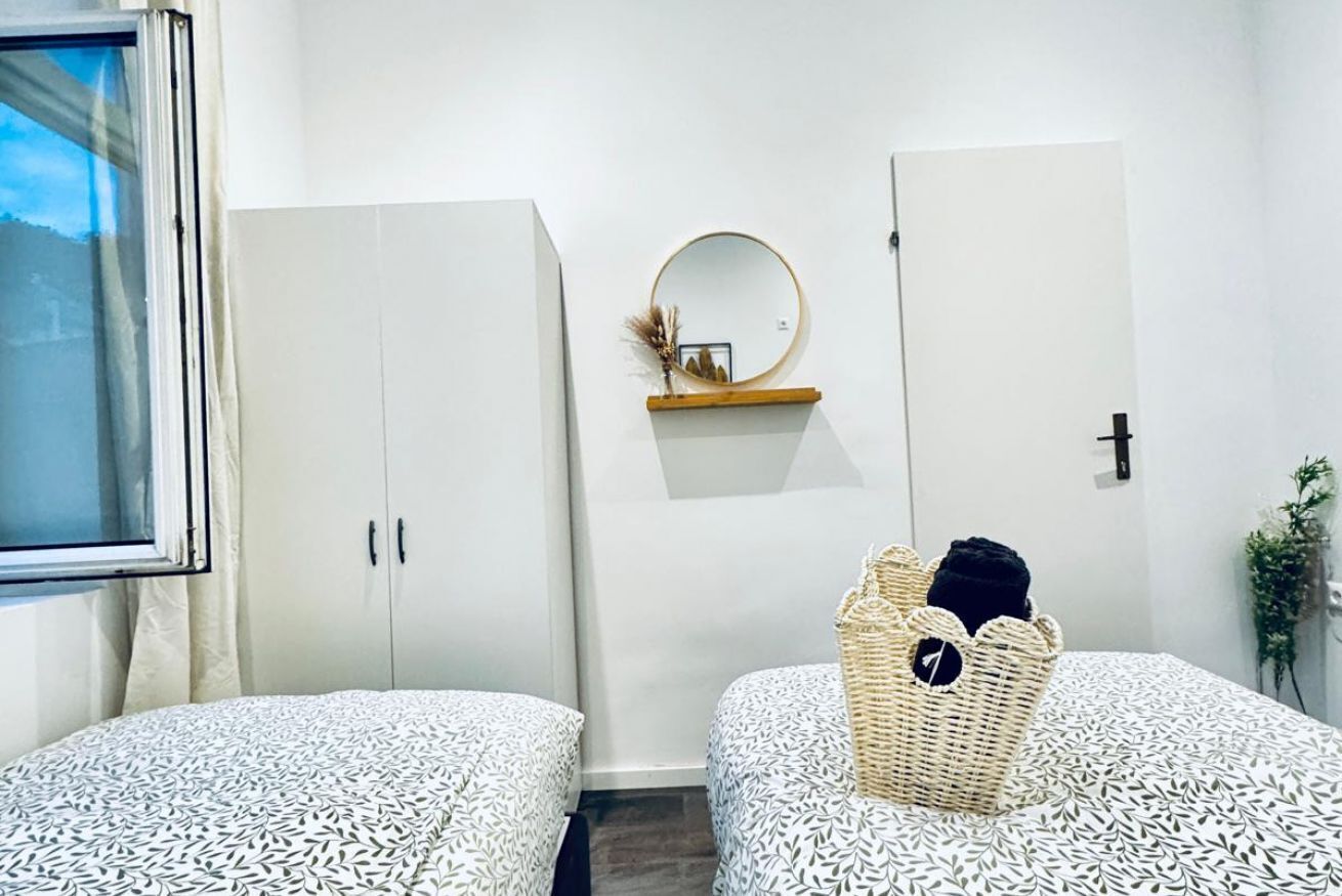A bedroom with two beds, a wardrobe, a mirror, and a small shelf with a picture frame.