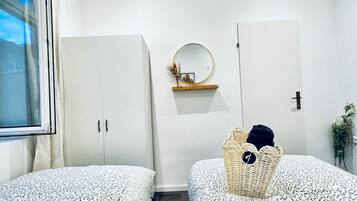 A bedroom with two beds, a wardrobe, a mirror, and a small shelf with a picture frame.