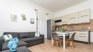 A modern apartment with a grey sofa, a dining table with chairs, a kitchen with white cabinets, and artwork on the walls. - 'Eleven Holidays Home' Apartment with Balcony, Wi-Fi and Air Conditioning (Catania)