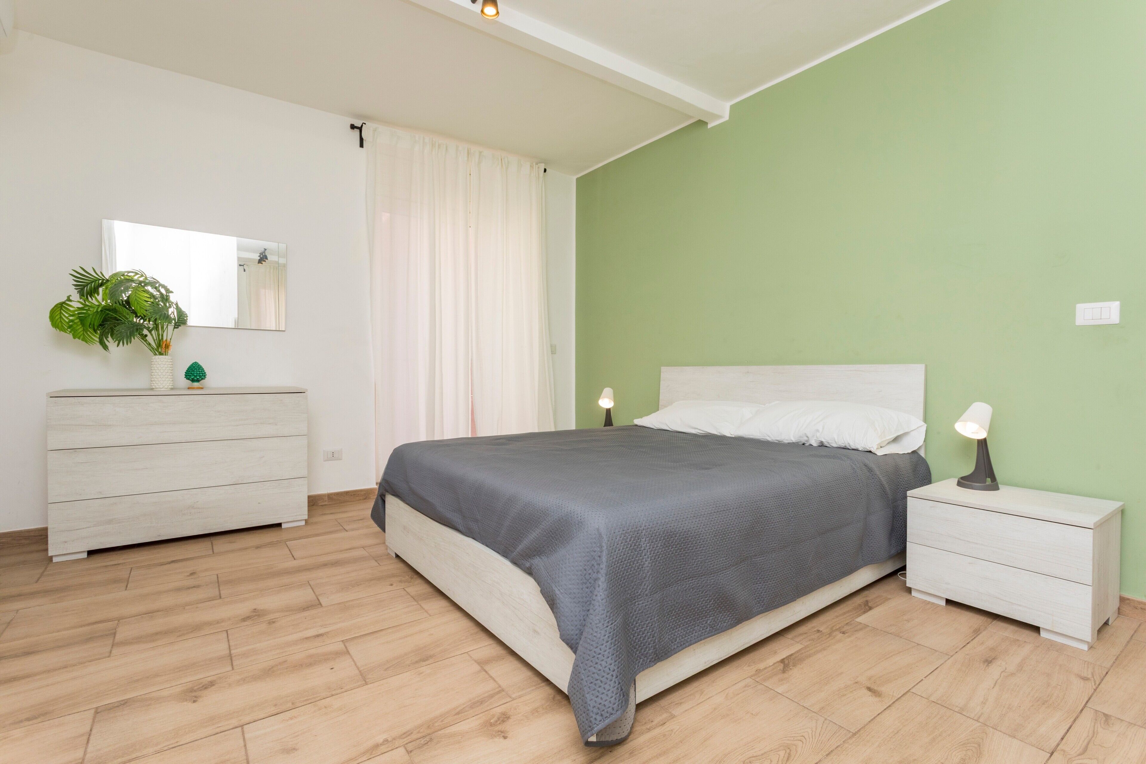 Une chambre à coucher comprenant un lit, une table de chevet, une commode, un miroir et une plante.