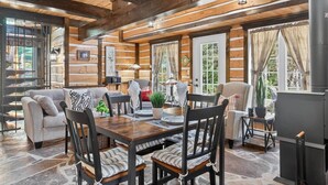 A cozy cabin interior with a wooden dining table, chairs, and a sofa. - Domaine Rivière Sacacomie - La Mésange (Saint-Alexis-des-Monts)