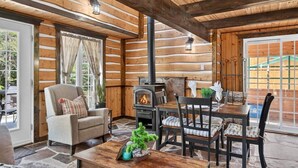 A cozy cabin interior with a fireplace, wooden walls, and a dining area. - Domaine Rivière Sacacomie - La Mésange (Saint-Alexis-des-Monts)