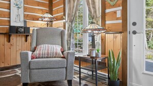 A cozy room with a grey armchair, a small table with a lamp, and a potted plant. - Domaine Rivière Sacacomie - Le Pic-Bois (Saint-Alexis-des-Monts)