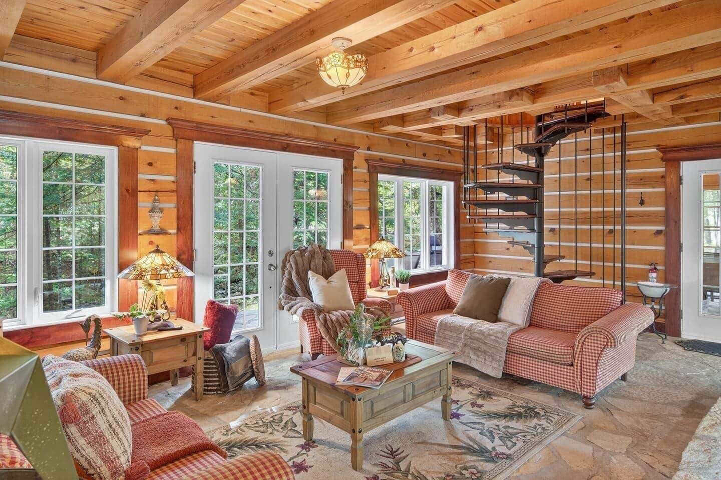 A log cabin interior with a checkered sofa, a wooden coffee table, and a spiral staircase.