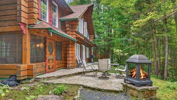 A log cabin with a stone patio, outdoor seating, and a fire feature.