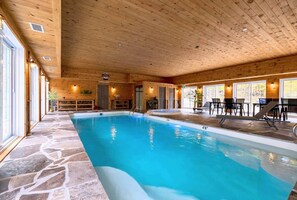 An indoor swimming pool with stone flooring, wooden walls, and a seating area with tables and chairs. - Domaine Rivière Sacacomie - Le Huard (Saint-Alexis-des-Monts)