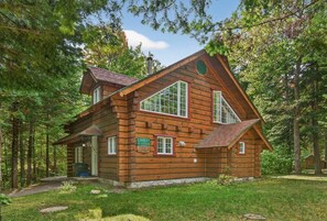 A log cabin with a steeply pitched roof, large windows, and a chimney.