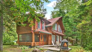 A log cabin with a stone fireplace, surrounded by a forest.
