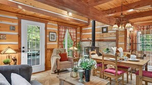 A cozy cabin interior with a stone fireplace, wooden furniture, and large windows. - Domaine Rivière Sacacomie - L'Aigle Royal (Saint-Alexis-des-Monts)
