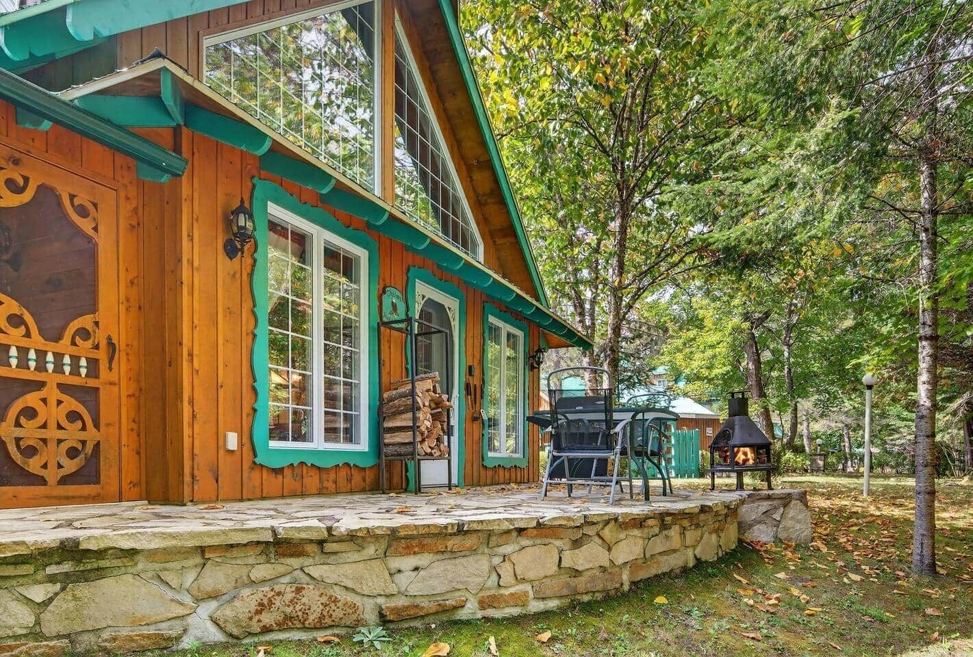 A wooden cabin with a stone foundation, large windows, and a covered porch area.