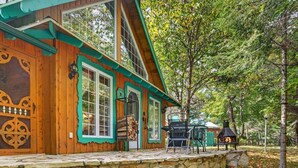 A wooden cabin with a stone foundation, large windows, and a covered porch area. - Domaine Rivière Sacacomie - L'Aigle Royal (Saint-Alexis-des-Monts)