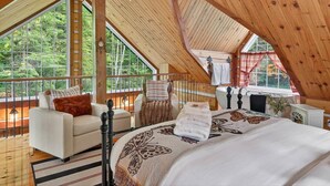 A bedroom with a large bed, a chair, a small table, and a window with a view of trees. - Domaine Rivière Sacacomie - L'Aigle Royal (Saint-Alexis-des-Monts)