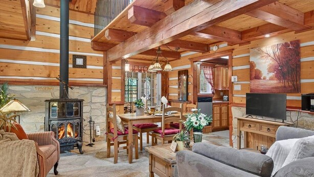 A cozy log cabin interior with a stone fireplace, wooden furniture, and a television. - Domaine Rivière Sacacomie - L'Aigle Royal (Saint-Alexis-des-Monts)