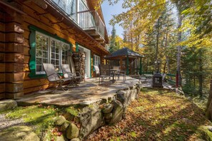 Une cabane en rondins avec un porche, des sièges d’extérieur et une vue sur une forêt.