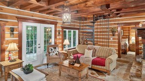 A log cabin interior with a wooden ceiling, a sofa, a chair, a table, and a lamp. - Domaine Rivière Sacacomie - L'Hirondelle (Saint-Alexis-des-Monts)