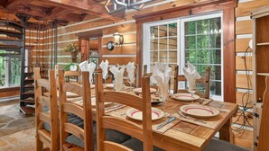 A wooden dining table set with plates, glasses, and napkins, surrounded by chairs. - Domaine Rivière Sacacomie - L'Hirondelle (Saint-Alexis-des-Monts)