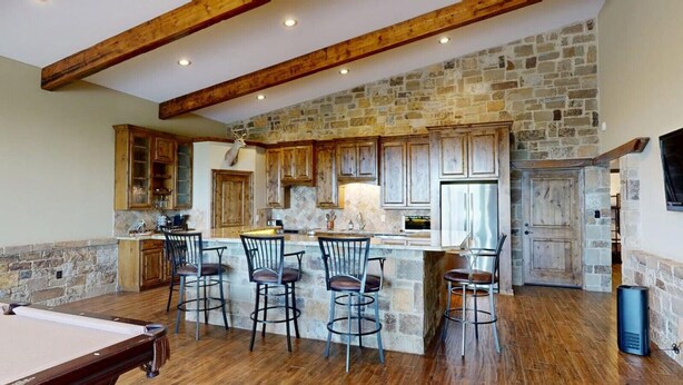A spacious kitchen with stone walls, wooden beams, and a central island with bar stools.