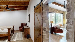 A rustic interior with a wooden bed, a leather armchair, and a stone wall.