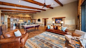 A spacious living area with a pool table, leather sofas, and a patterned rug.