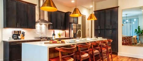 Una cucina moderna con mobili scuri, un'isola centrale con sgabelli da bar, illuminazione a sospensione e un frigorifero in acciaio inossidabile.