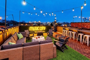 An outdoor seating area with a neon sign, wicker furniture, and string lights. - Luxury Retreat Double Rooftop Deck Game Room (Nashville)