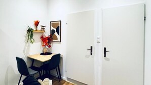 Une pièce avec une porte blanche, une petite table entourée de chaises, une plante et un tableau encadré accroché au mur.