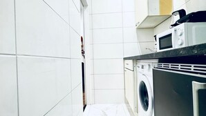 Une cuisine compacte aux murs recouverts de carreaux blancs, équipée d’un lave-linge et d’un four à micro-ondes.