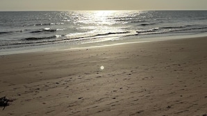 Ein Strand mit blauem Himmel und der Sonne, die auf dem Wasser glitzert.