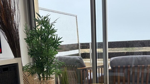 Ein runder Tisch mit dekorativen Elementen, einer Obstschale und Blick auf den Strand durch große Fenster.