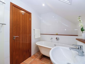 A bathroom with a wooden door, white tiles, a bathtub, a sink, and a small shelf with a plant. - Heathcliffe House (Cardiff)