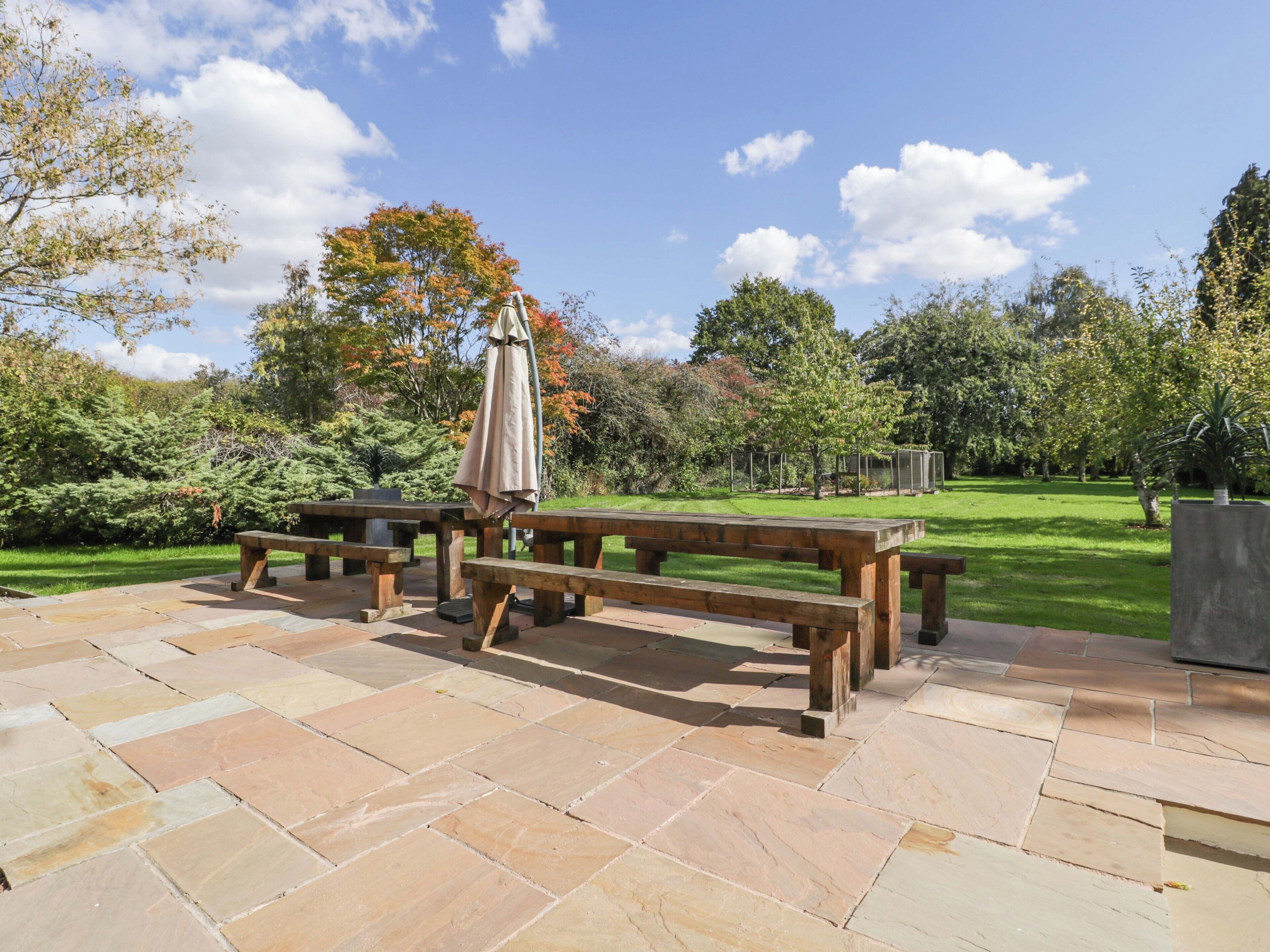 An outdoor patio with stone flooring, wooden benches, and a picnic table.