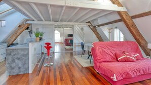 Habitación estilo loft con techo de madera, un sofá rojo, una zona de cocina y una mesa de comedor.