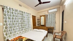 A bedroom with a bed, a wooden chair, a desk, a mirror, and a ceiling fan. - Sri Mayapur Chandrodaya Guest House (Krishnanagar)