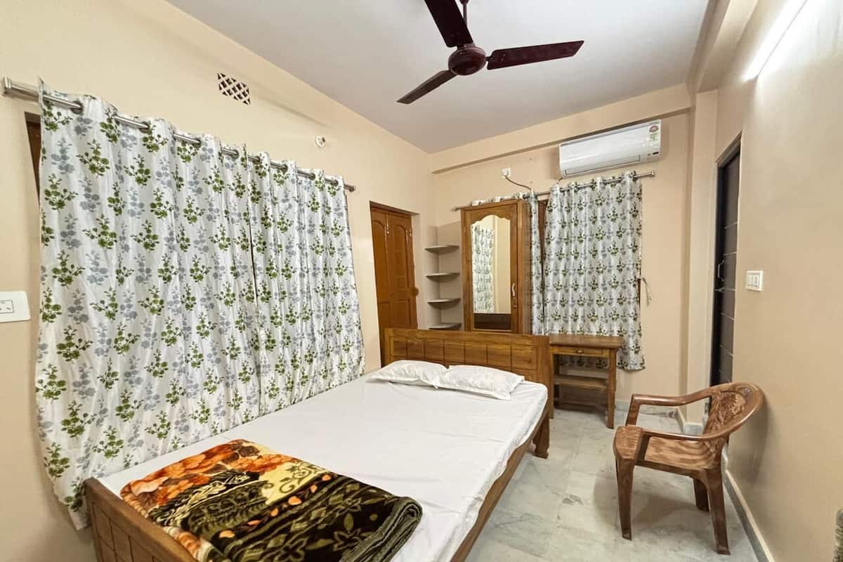 A bedroom with a bed, a wooden chair, a desk, a mirror, and a ceiling fan.