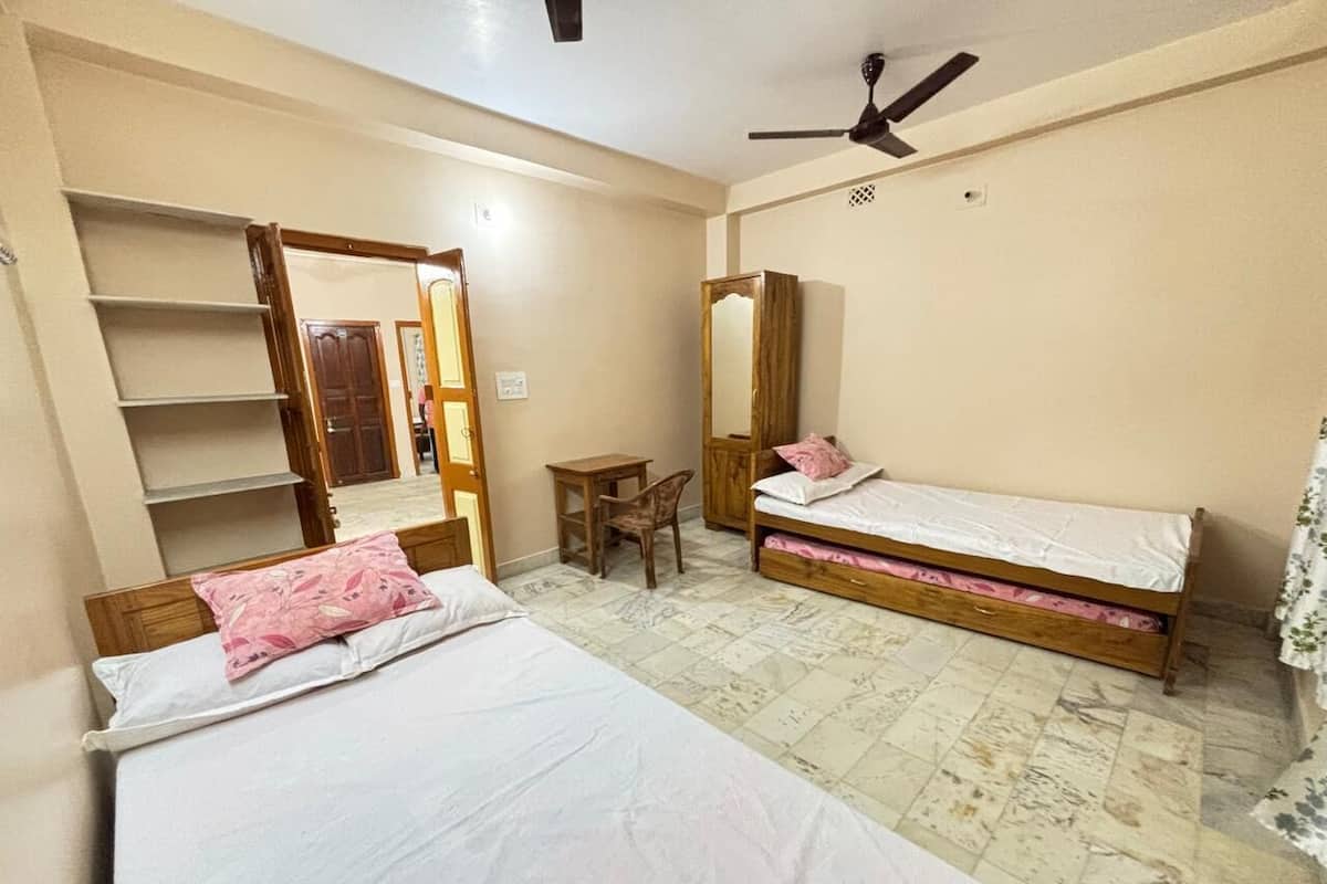 A bedroom with two single beds, a wooden wardrobe, a small table, and a ceiling fan.