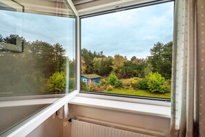 A window with a view of a garden and a small blue building.