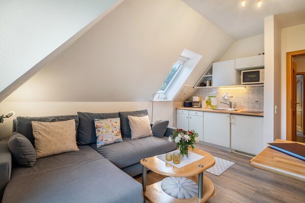 Un espacio habitable moderno estilo loft, con techo inclinado, un conjunto de sofás, una zona de cocina y una pequeña mesa de comedor.