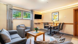 Un salon moderne comprenant un canapé, une table basse avec un vase, un coin repas avec des chaises, un téléviseur fixé au mur et un tableau.