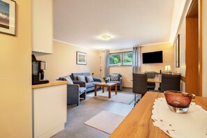 A compact living space with a kitchenette, a sofa, a dining table, and a TV mounted on the wall.