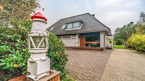 Une maison avec une allée pavée, une structure blanche ressemblant à un phare et un chemin en briques.