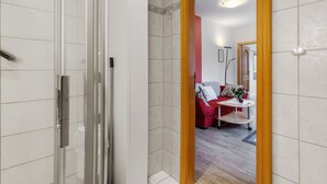 A modern bathroom with a glass shower enclosure, a white tiled wall, and a wooden door frame. - Apartment 'Karroo' with Shared Garden and Wi-Fi (Wittdün)