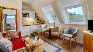 A compact living space with a kitchenette, a dining area, a sofa with floral cushions, and a television on a wooden cabinet. - Apartment 'Karroo' with Shared Garden and Wi-Fi (Wittdün)