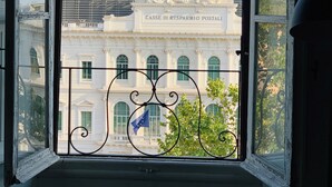 Ein offenes Fenster mit Blick auf ein Gebäude, das eine Plakette mit der Aufschrift "Casse di Risparmio Postali" und eine Flagge der Europäischen Union zeigt.