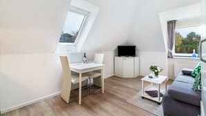 Habitación moderna y bien iluminada con una mesa de comedor, un sofá, un televisor y una ventana con vistas a árboles.
