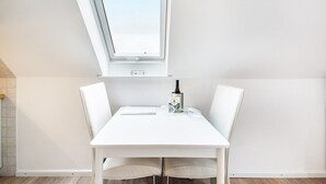 Una mesa de comedor blanca con dos sillas, una botella de vino y una copa sobre la mesa.