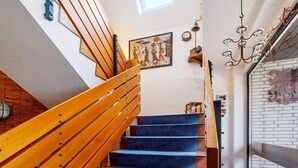 Una escalera con barandillas de madera y peldaños cubiertos de moqueta azul, un reloj fijado a la pared y un candelabro.