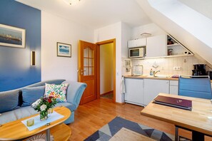 A compact living space with a kitchenette, a sofa with a floral cushion, a dining table, and a wooden floor.