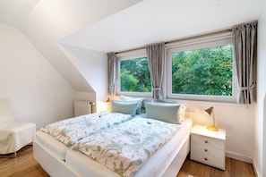 A bedroom with a bed, two bedside tables, a chair, and a window with curtains.