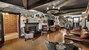 A cozy, rustic lounge area with a brick wall, leather seating, a fireplace, and a large TV screen.