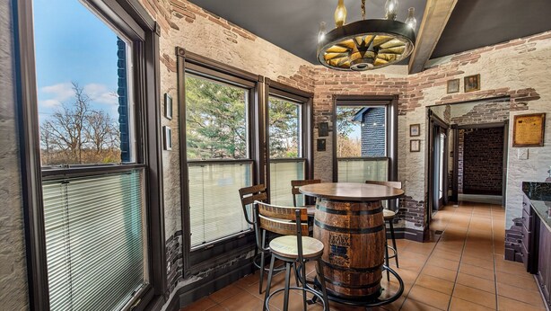 A rustic interior with a large window, a round wooden bar, and a chandelier.